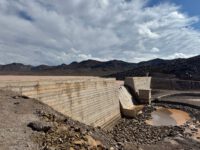 Stunning view of a concrete dam set against a mountainous and arid landscape, under a clear blue sky.